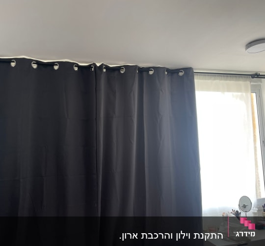 וילון כהה תלוי על מוט ליד חלון מואר